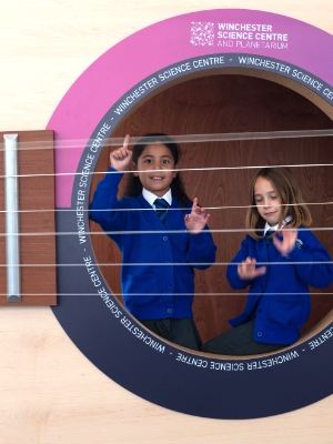 Interactive science exhibition photo showing two school children inside the giant guitar