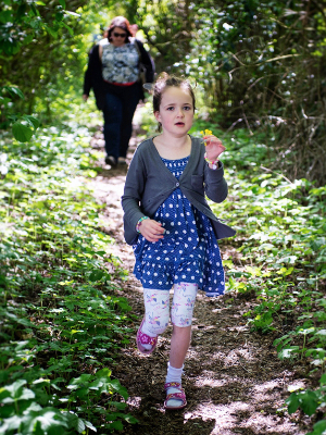 A young girl walking through woodland towards the camera, holding a flower