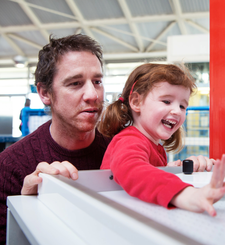 Interactive science exhibition photo showing a young girl and her dad smiling and engaging with an exhibit