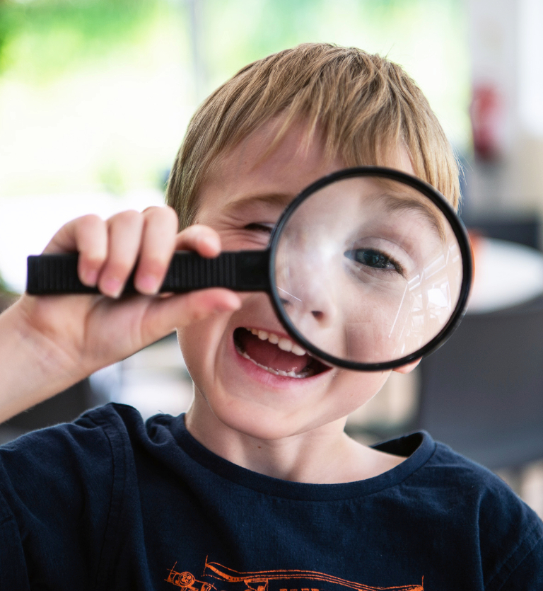 A young boy laughs as he peers through a magnifying glass