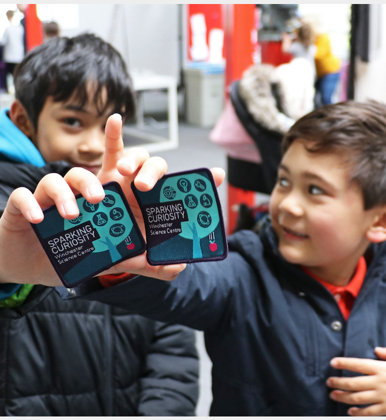 Two boys holding up their Curiosity Badges to the camera and smiling