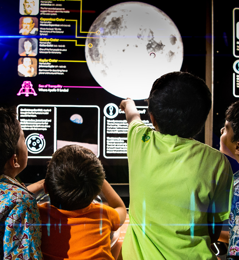 Four children pointing at the moon displayed on a lit up panel in the Science Centre exhibition