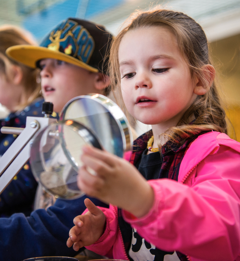 A young girl studies a scientific sample through a magnifying glass