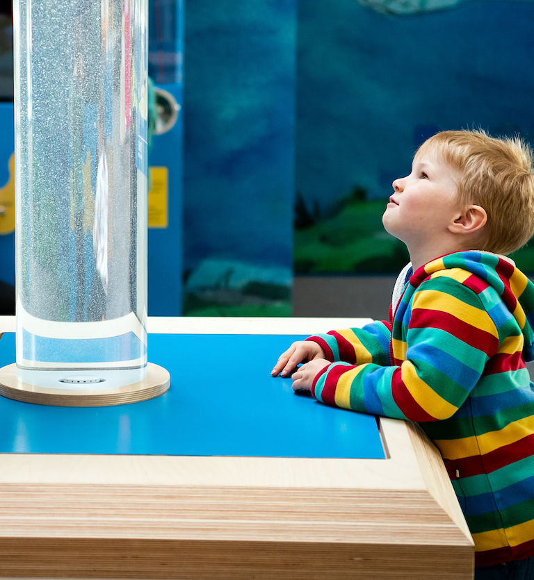 Interactive science exhibition photo showing a young boy looking up in wonder at bubbles in a tube