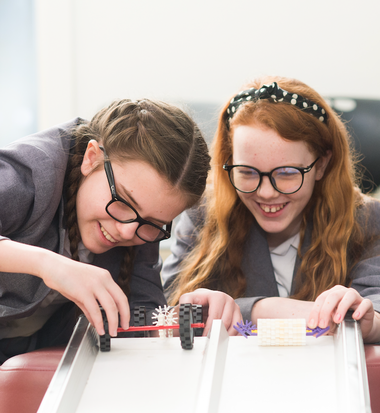 Two school pupils smiling while engaging with a STEM-related activity