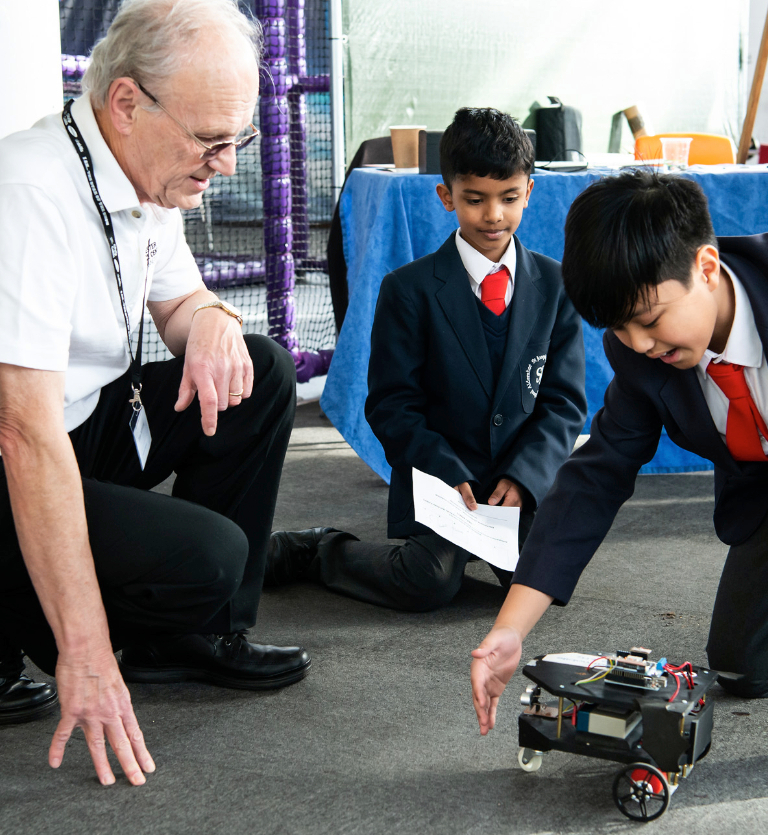Two school children and a male member of staff crouched down testing a robot