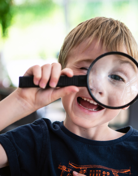 A young boy laughs as he peers through a magnifying glass