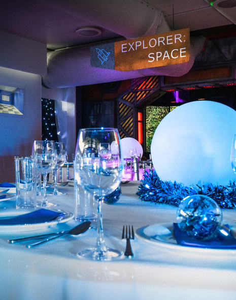 A dinner table with white tablecloth set up for Christmas dinner with space items in the background