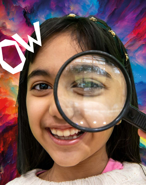 A girl hold a magnifying glass over her eye and smiles