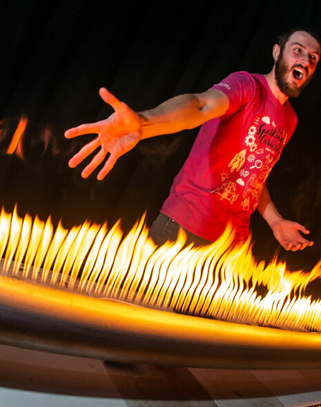 A man stands behind a tube with lots of flames coming from it