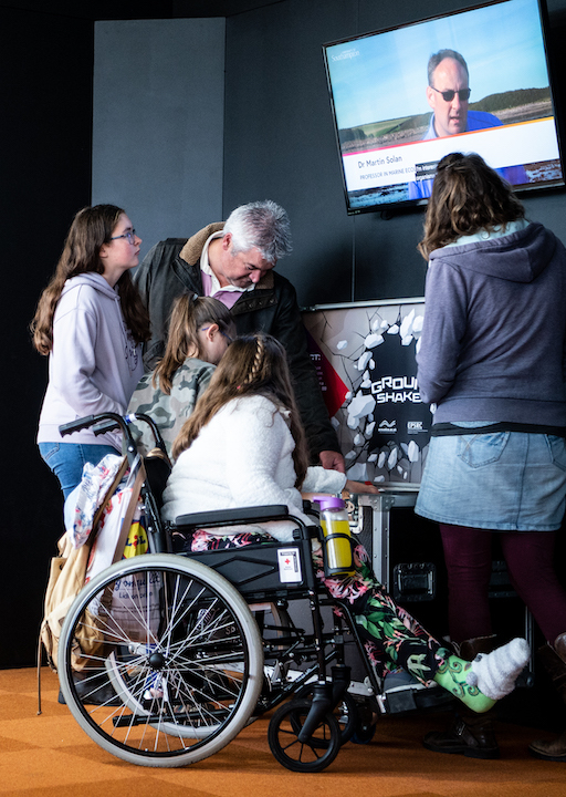 Interactive science exhibition photo showing a family engaging with an exhibit, with one of the children in a wheelchair