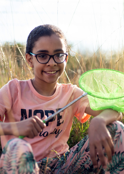 A little girl holds a butterfly net sitting in a field