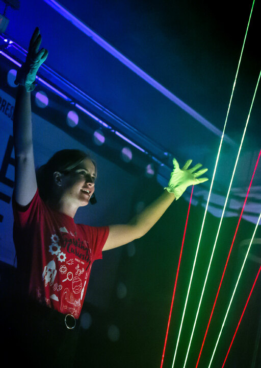 A woman waves her arms in the air in front of beams of coloured light