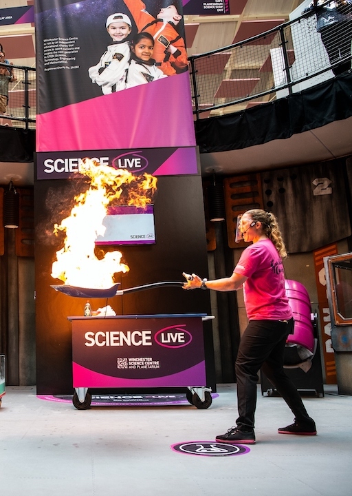 Live science demo area photo showing a presenter holding a spade with some liquid that has been set on fire