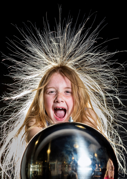 A girl laughs as her hair stand on end while using a van de graaf science experiment