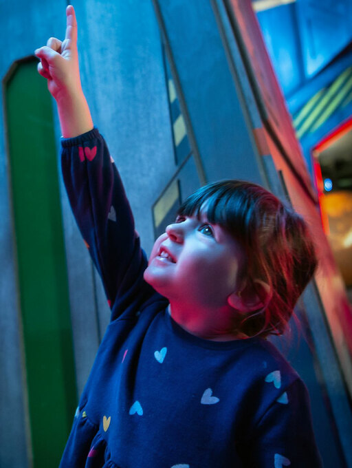 A woman waves her arms in the air in front of beams of coloured light